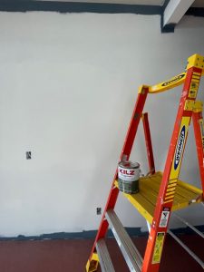 Paint ladder with gallon pail of Kilz and white wall behind