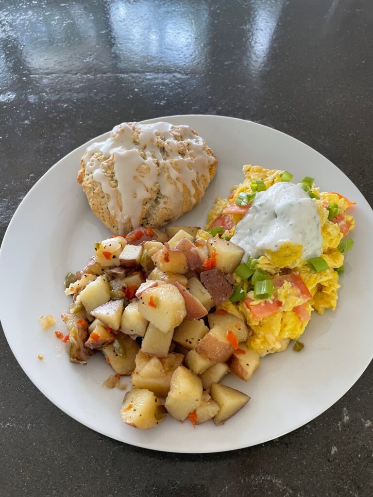White plate with hash brown potatoes, eggs with salmon, and lemon poppy seed scone