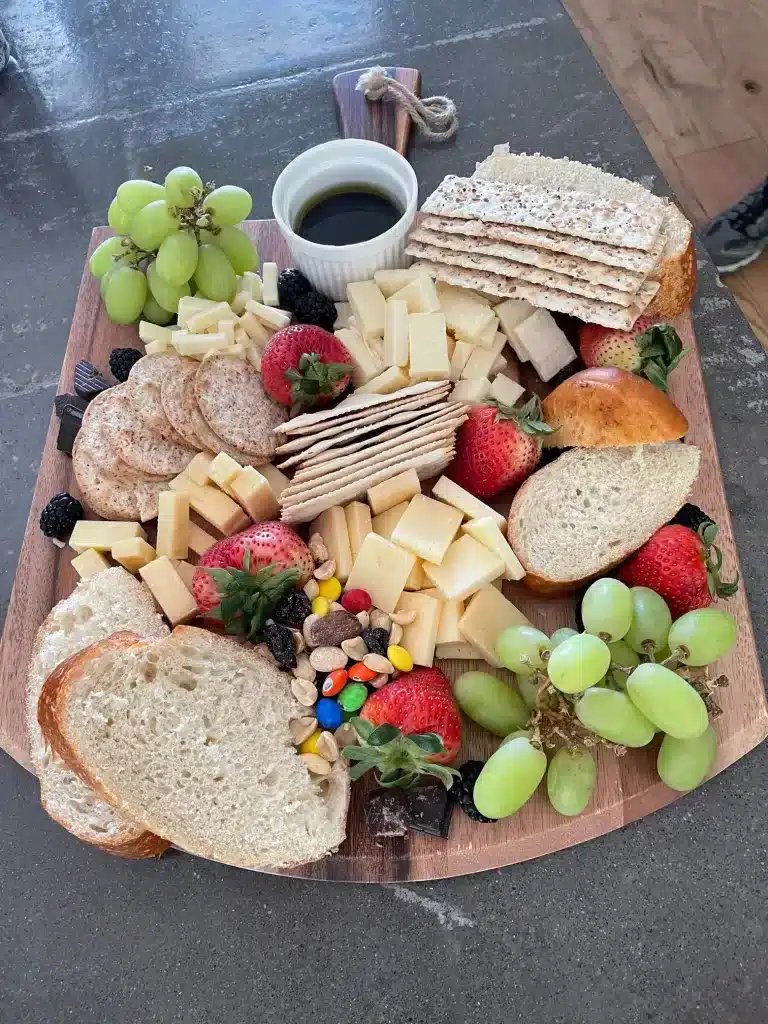 Charcuterie platter with grapes, bread, strawberries, crackers, dipping sauce,, and cheese