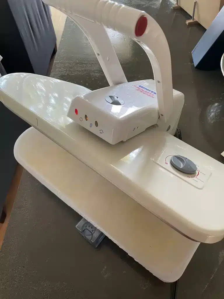 White brand clothes steam press perched open on a cement kitchen island