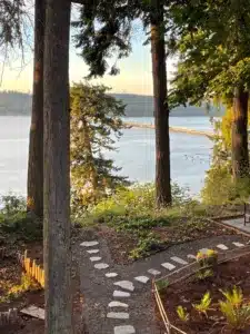 Pretty scene looking out at water with bridge in background and stepping stone path in foreground with several mature Douglas fir trees