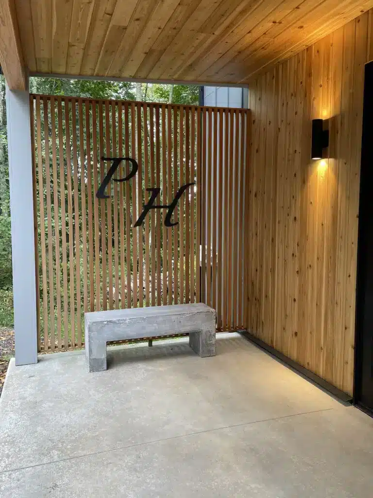 Front porch with cement bench, black sconce light, and prominent "P" and "H" letters in black mounted on cedar slat wall over bench