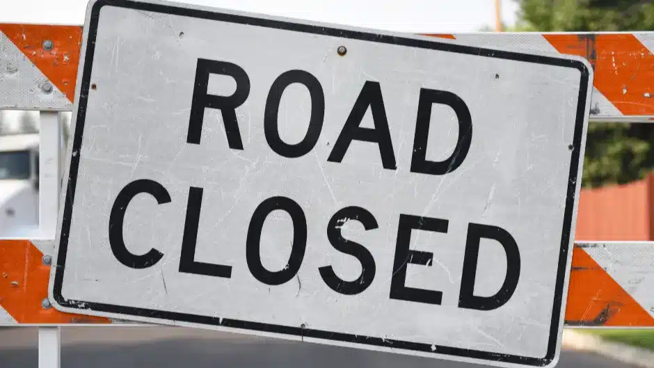 White "Road Closed" sign with black lettering in front of orange caution barrier